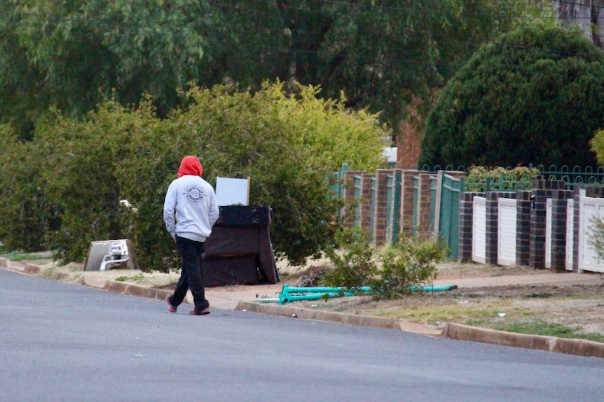 A man wearing a hooded jumper walks away from the camera.