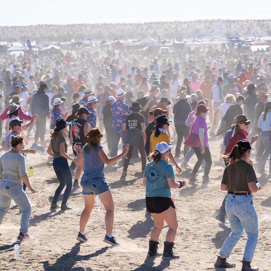 A wide shot of thousands of people dancing in lines in dust.
