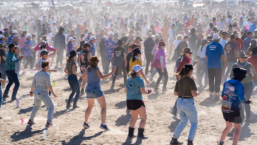 A wide shot of thousands of people dancing in lines in dust.