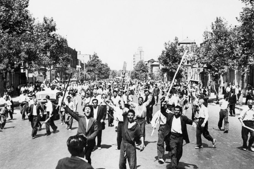 Black and white old photo of demonstrators marching with staves and showing slogans during riots in Tehran, August 1953.