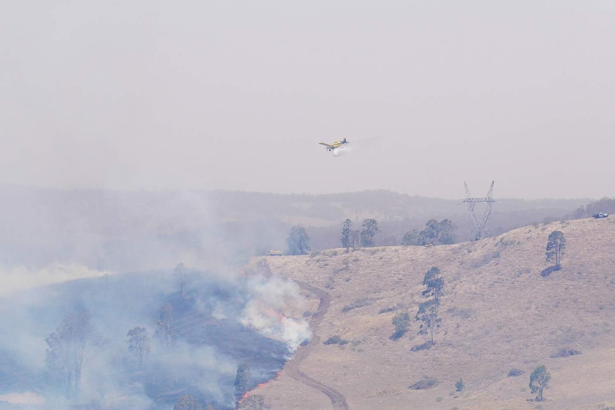 A plane flies over a burning hillside