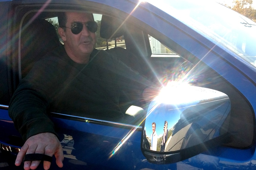 Ross Lyon driving a car while wearing sunglasses, with his arm out the window.