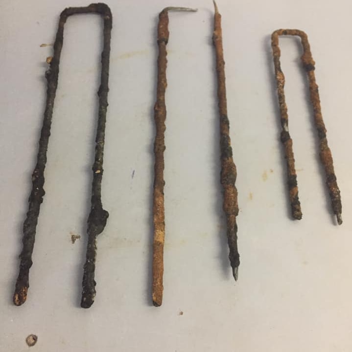 Three rusted metal spikes place on a white table.