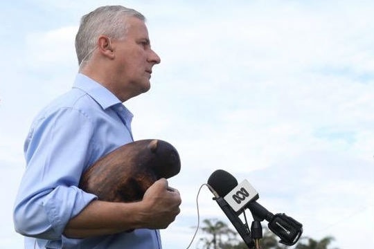 Michael McCormack, with a wooden wombat tucked under his arm, stands in front of a microphone.