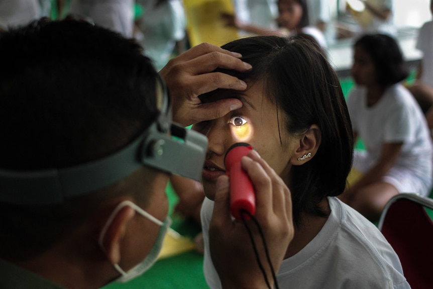 Officer conducts an eye examination of a female army candidate.
