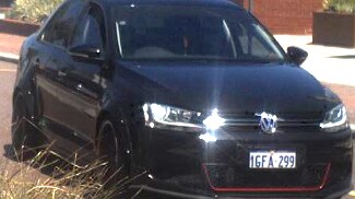 A black car with a red stripe on the front driving down a road.