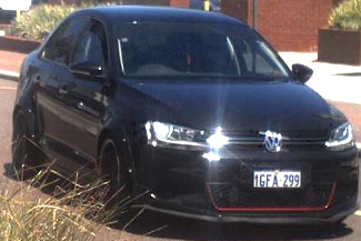 A black car with a red stripe on the front driving down a road.