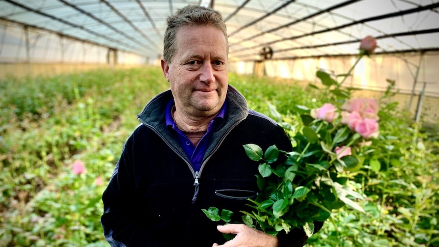 A man looks into the camera, holding a bouquet of roses.