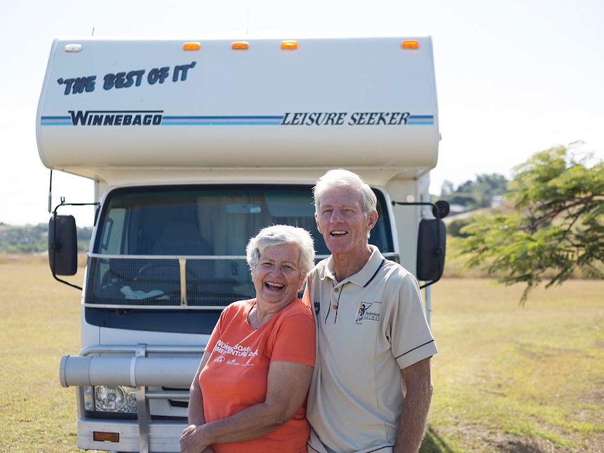 An older couple stand in front of their motor home with arms around each other smiling.