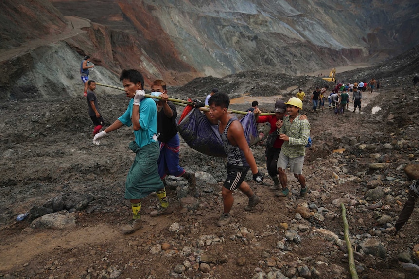 Rescue workers use poles to carry a body shrouded in blue and red plastic sheet through a muddy mountain area.