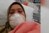 A photo of a woman wearing a mask in a hospital bed. 