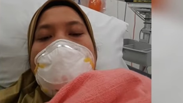 A photo of a woman wearing a mask in a hospital bed. 