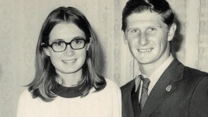 photograph of woman and man smiling at camera, man has hands around her waist