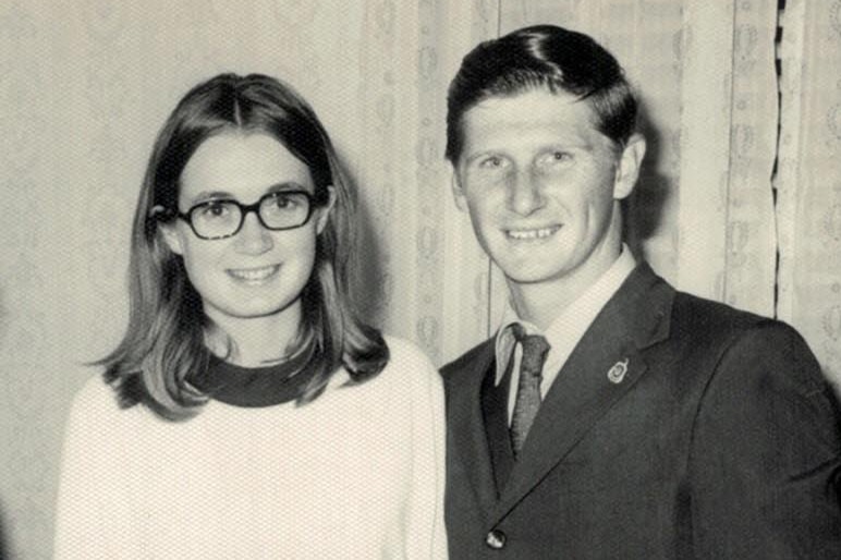 photograph of woman and man smiling at camera, man has hands around her waist