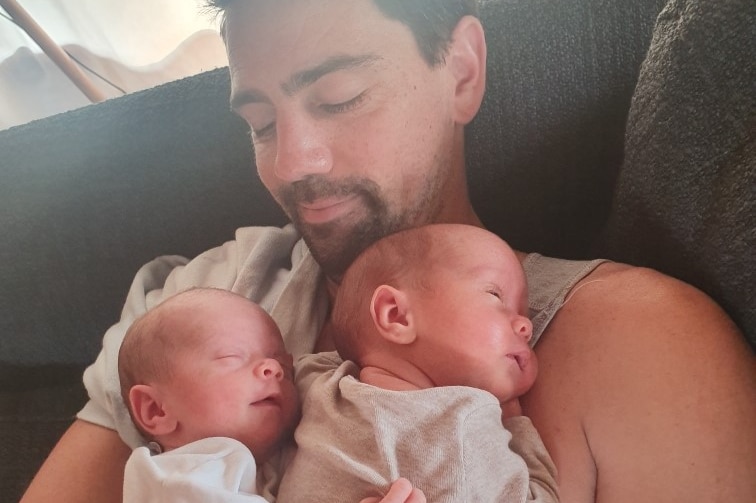 A man sits on a chair holding his newborn twins