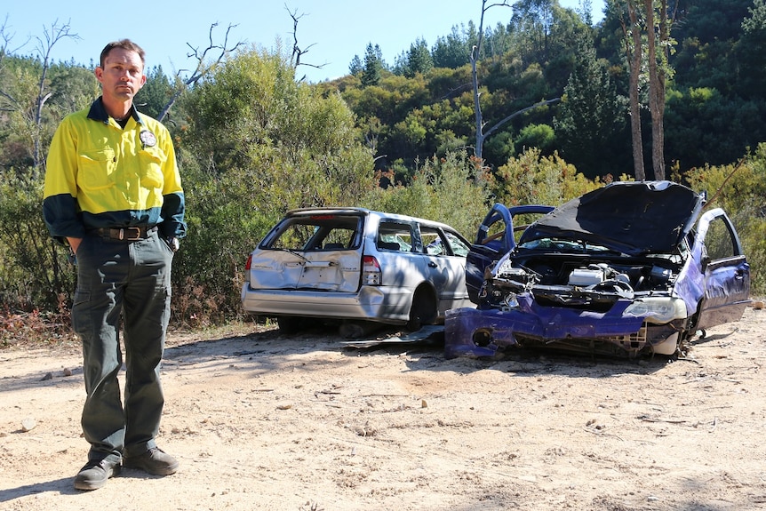 Marty Bajt stands in front of two smashed cars.