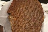 The half-broken clay tablet fragment is covered in ancient cuneiform script.