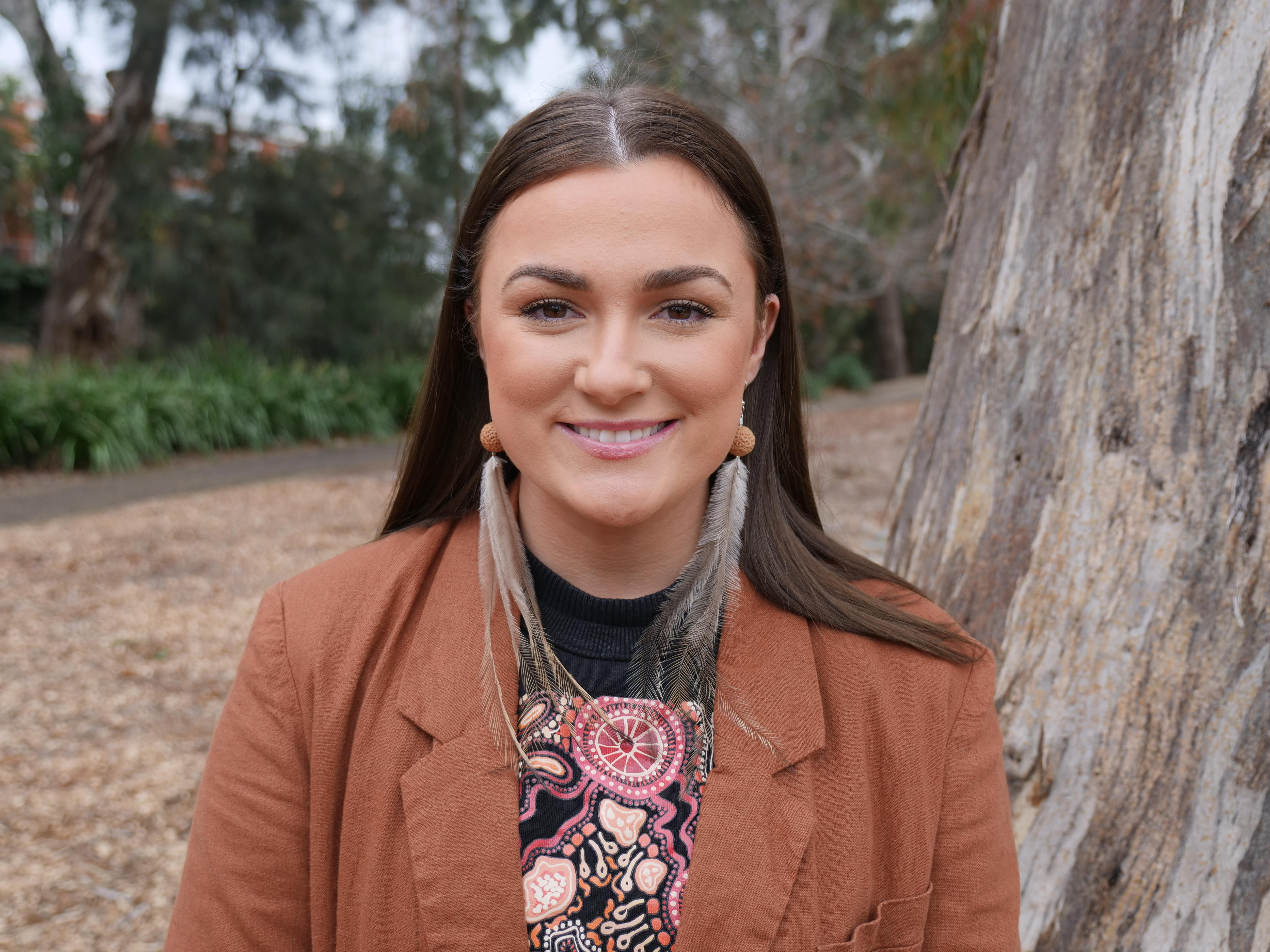 A woman smiling and wearing quandong and emu feathers. 