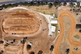 A birds eye view of a red dirt track, cars, buildings and trees