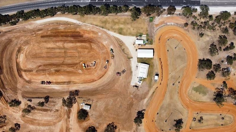 A birds eye view of a red dirt track, cars, buildings and trees