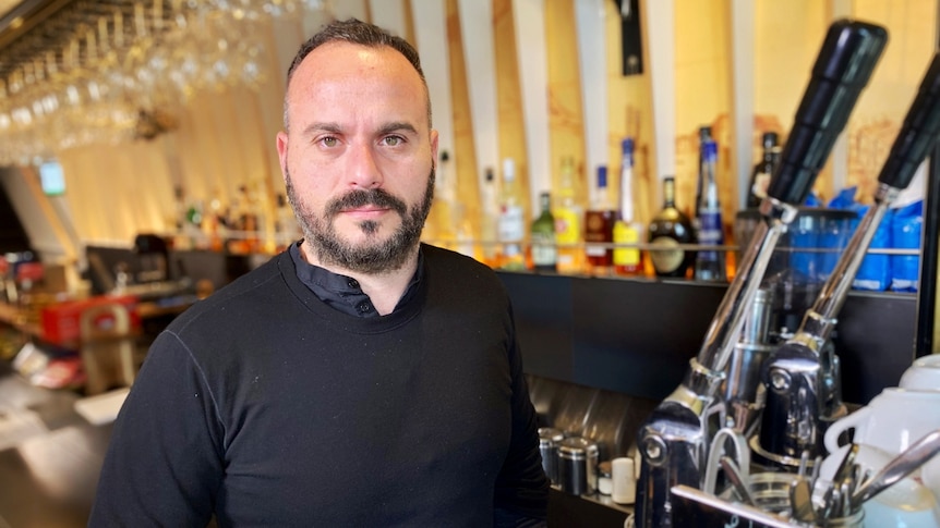 Stavros Konis wearing all black and standing next to an espresso machine.