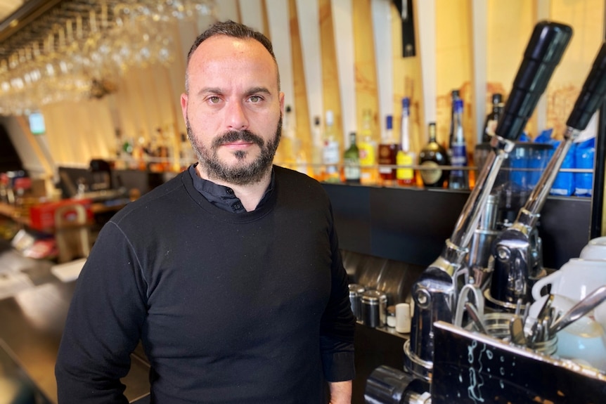 Stavros Konis wearing all black and standing next to an espresso machine.