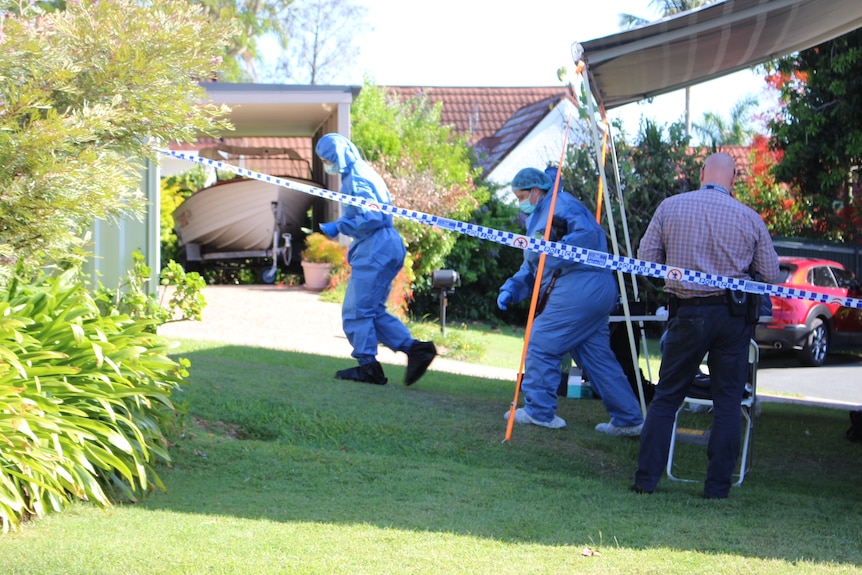 A cordoned off area in a suburban garden sees two workers in blue medical suits walk across grass