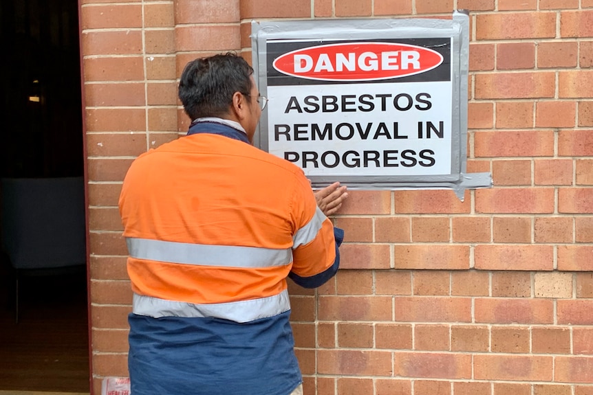 Man putting up sign "Asbestos Removal in Progress"