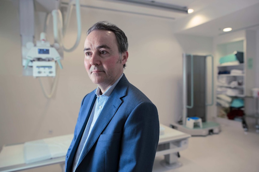 A close up portrait of a man in a suit in front of an X-ray machine