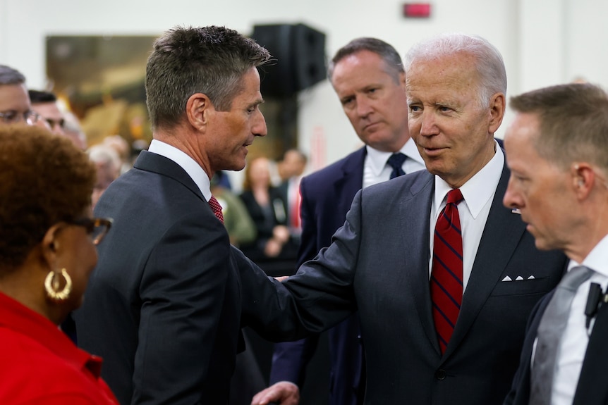 Joe Biden touches another man in a suit on the arm as they greet.  