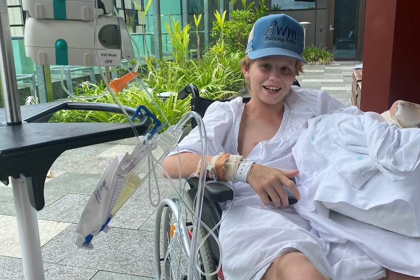 A boy in a hospital gown smiles from a wheelchair.