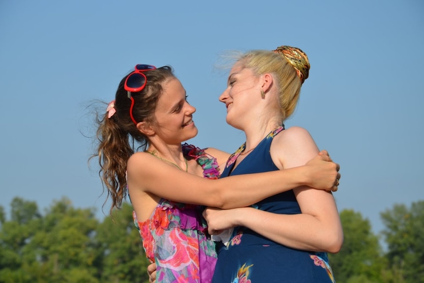 Two women hug outdoors looking each other in the eyes happily.