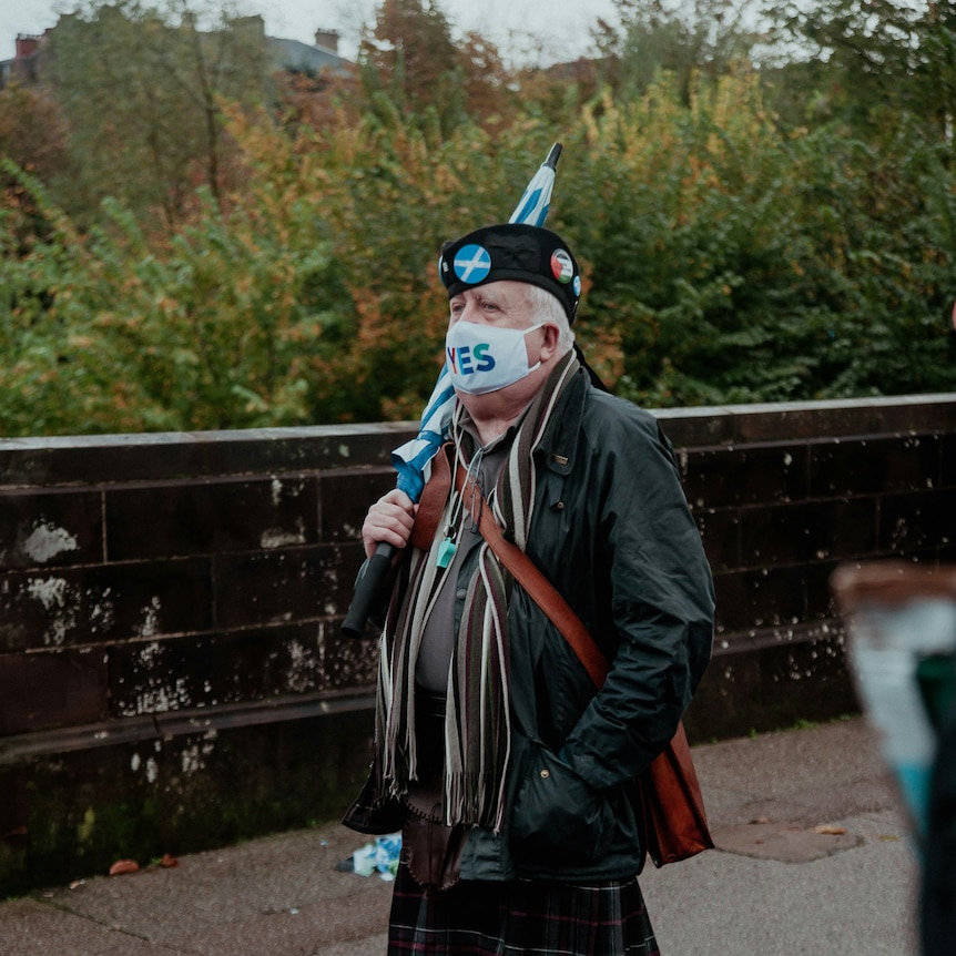 Man in a kilt wearing political badges and a pro-Scottish independence facemask. 
