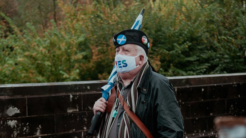 Man in a kilt wearing political badges and a pro-Scottish independence facemask. 