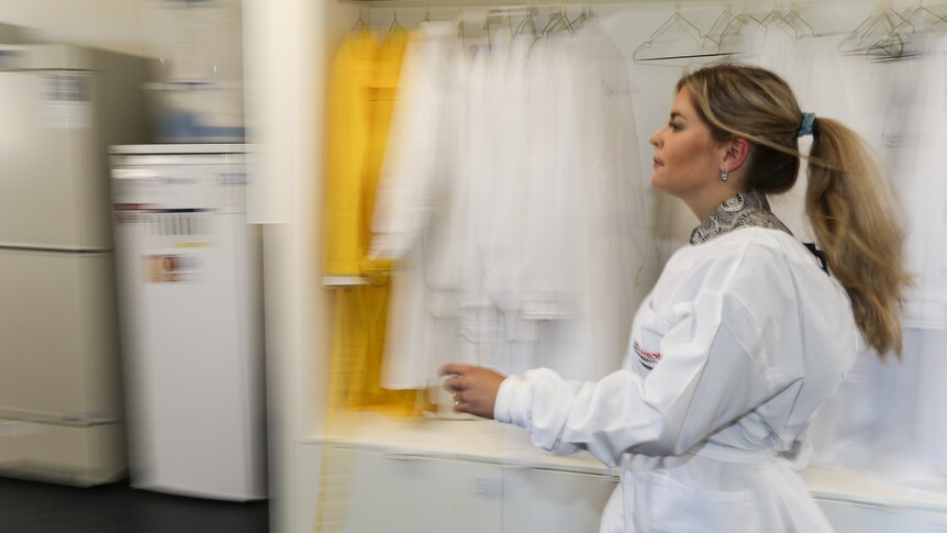 Environmental biologist Marianne Haines walking past a row of white lab coats.