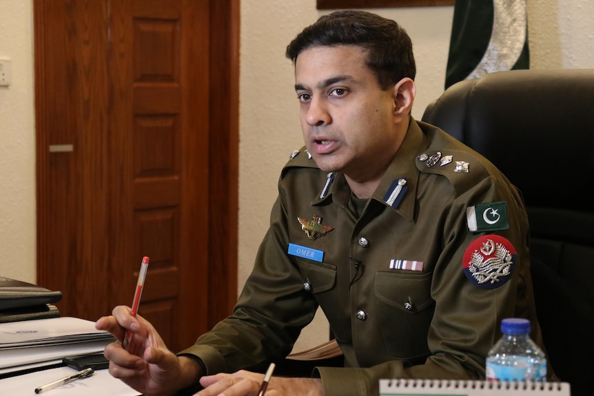 A Pakistani police officer holding a pencil sits at a desk looking contemplative
