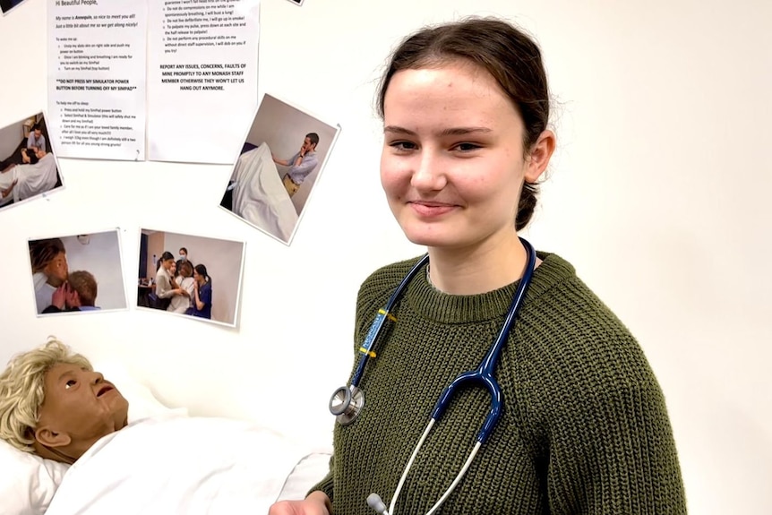 Dark haired girl smiling wearing a dark green knitted jumper and a stethoscope around her neck.