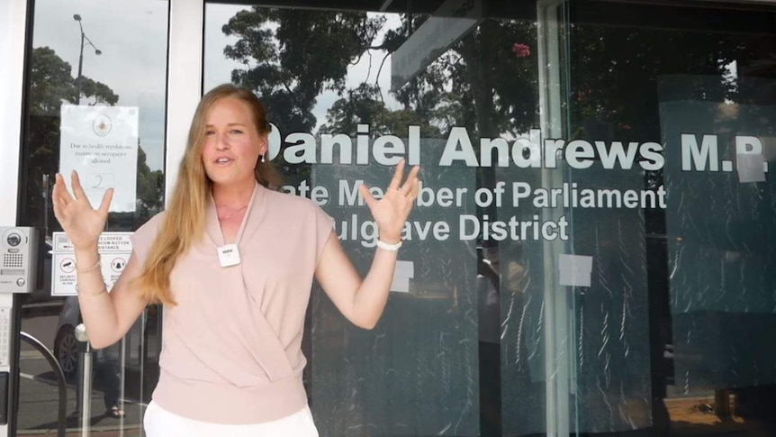 A woman in her early 30s raises her arms while giving a speech outside Dan Andrews' office