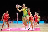 An Australian netballer leaps high and grabs the ball during a game as a number of England players look on.
