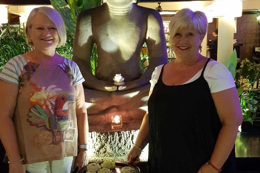 Two women in front of a Thai statue.