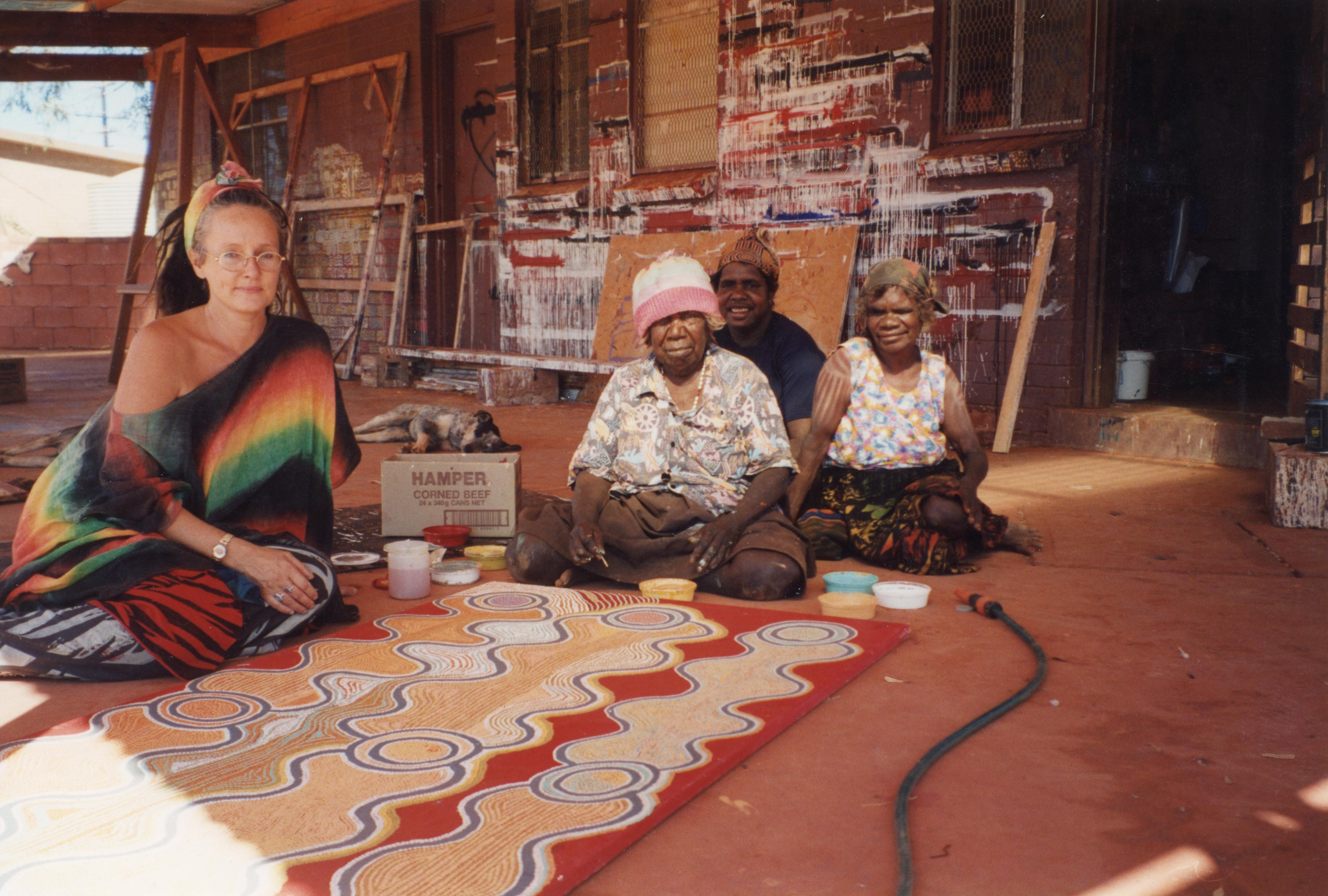 Woman sitting with Indigenous artists with their artwork in front of them.