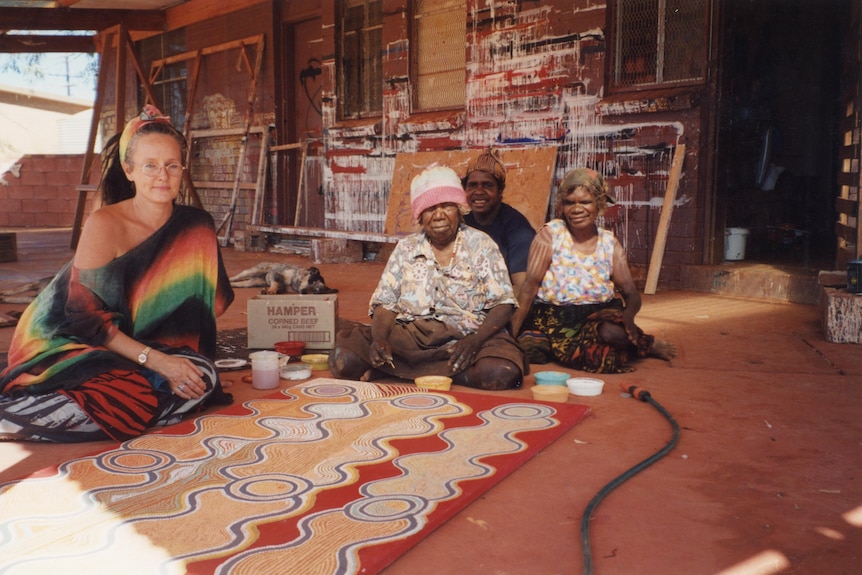 Woman sitting with Indigenous artists with their artwork in front of them.