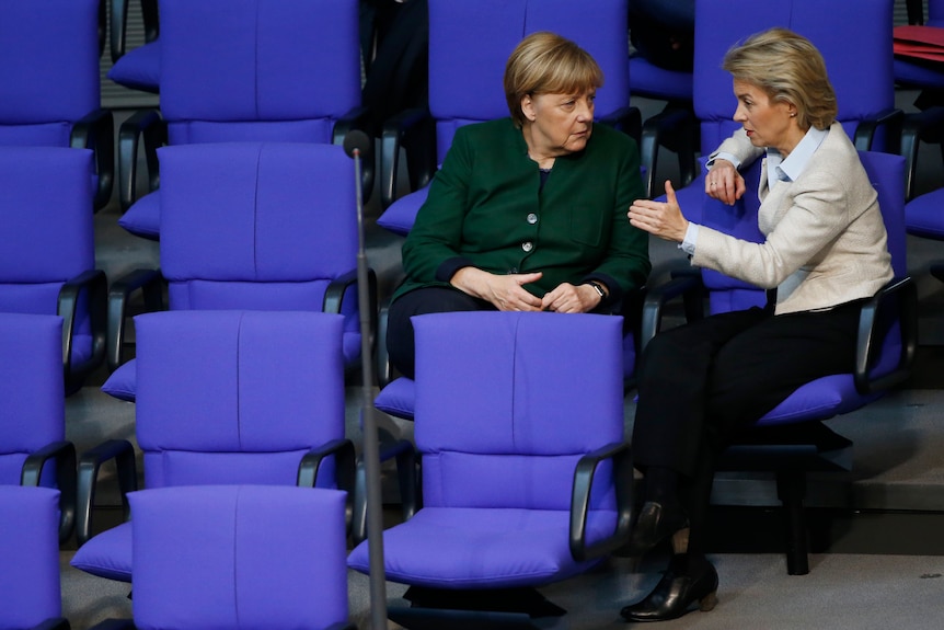 Angela Merkel and Ursula von der Leyen sit in blue chairs and are deep in conversation. 