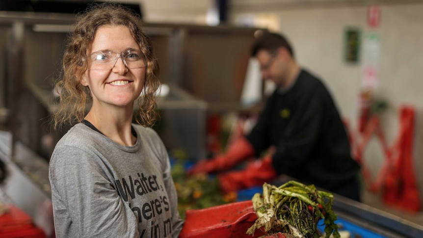 Women in safety goggles holding food waste on a production line. Man in the background, out of focus.