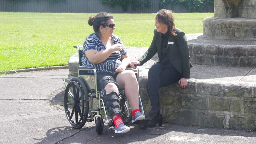 A woman in a wheelchair sits with her friend in a park.