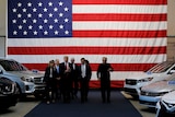 President Trump and company walk down a row of cars with large US flag in background
