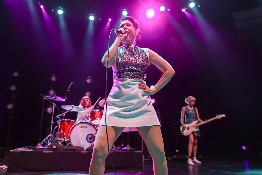 Bikini Kill perform at Hollywood Palladium. Kathleen Hanna is foregrounded, as she signs to the audience
