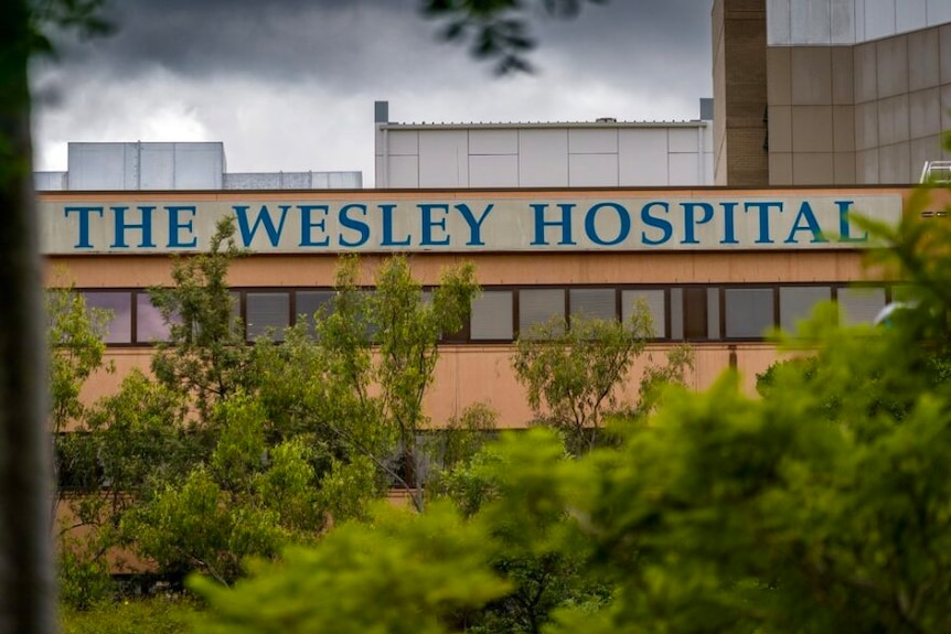 A sign on a building, partially obscured by trees, marks The Wesley Hospital.