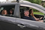 A mother driving a car with three children as passengers.