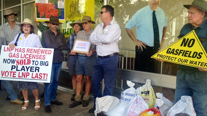 Farmers stand at front of MP's office holding ant CSG signs with manure at their feet.